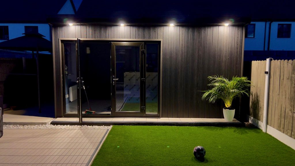 Dark-clad garden room lit at night with artificial grass in front